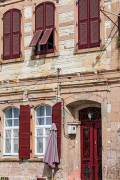 Traditional stone house facade with red wooden shutters and door in historic Aegean town