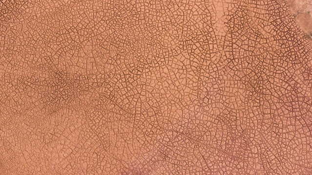Aerial view of the intricate cracked patterns of a dried salt lake bed in the outback, showcasing textured orange and brown earth formations in Kalbarri, Western Australia, Australia.