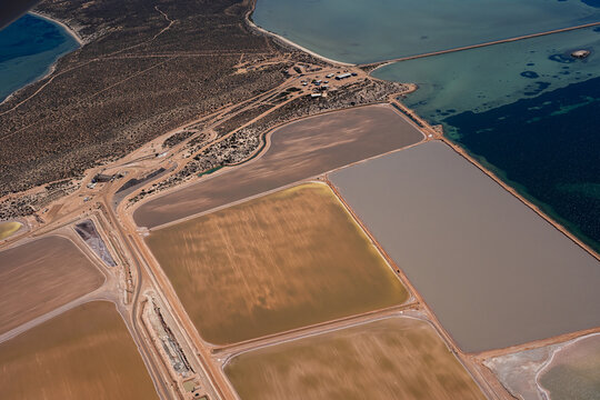 Aerial view of Useless Loop salt works with industrial evaporation ponds in shades of brown and yellow, surrounded by arid coastal terrain in Kalbarri, Western Australia, Australia.