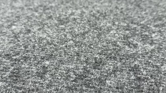 Close-up shot of a grey textured carpet mat with small white fibers. macro rug pattern, soft floor background, abstract durable textile surface, interior flooring details.