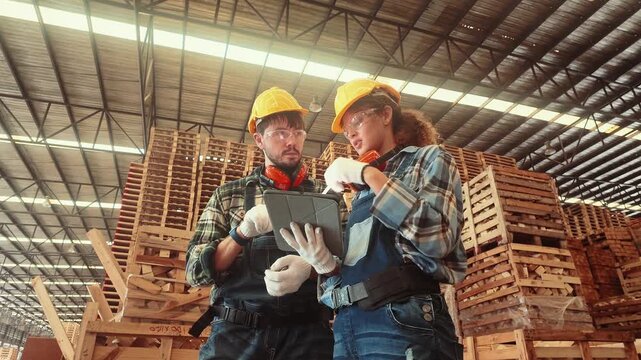 Workers check inventory in a warehouse while reviewing data on a tablet with storage pallets in the background