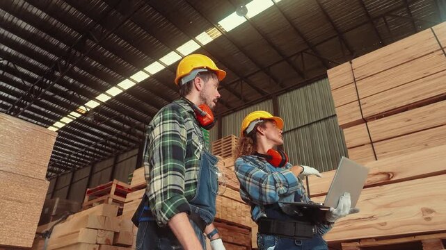 Workers use a laptop to discuss tasks at a lumber warehouse during the day