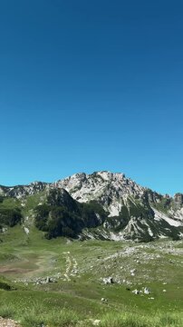 Vertical panorama shows rocky green slopes of Sedlo Pass in Durmitor Montenegro. Alpine summer scenery for hiking tourism adventure and travel