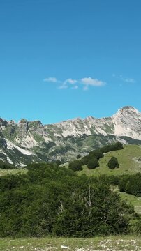 Vertical panorama shows rocky green slopes of Sedlo Pass in Durmitor Montenegro. Alpine summer scenery for hiking tourism adventure and travel