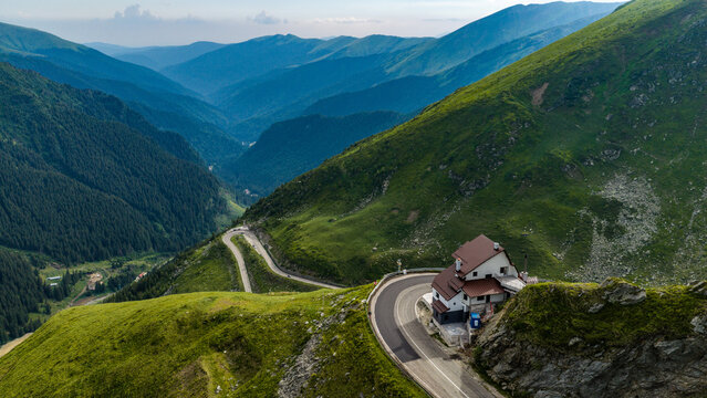 Aerial view of Transfagarasan mountain pass with its winding road and a mountain lodge nestled in the lush green Carpathian Mountains, Curtea de Arges, Judetul Arges, Romania.