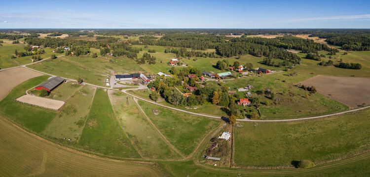 Aerial view of traditional red wooden farmhouses surrounded by sprawling green pastures, agricultural fields, and forests in the Swedish countryside in Rimbo, Stockholm County, Sweden.