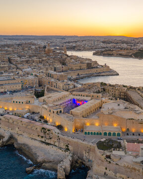 Aerial view of the historic Fort St. Elmo at sunset with golden light illuminating the stone fortifications and the surrounding urban skyline of Valletta, Port Region, Malta.