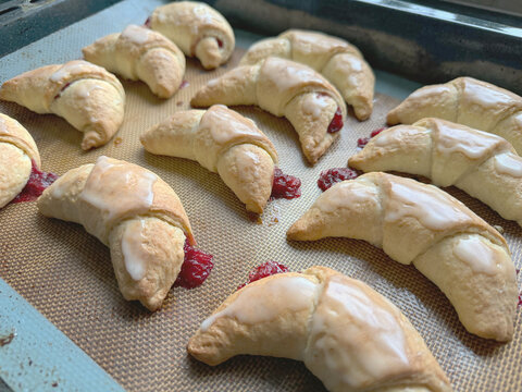 Freshly baked raspberry croissants arranged on baking tray with golden flaky pastry bright berry filling and smooth white glaze Homemade crescent shaped pastries showcase tender layers crisp edges swe