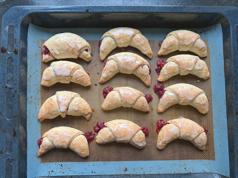 Freshly baked raspberry croissants arranged on baking tray with golden flaky pastry bright berry filling and smooth white glaze Homemade crescent shaped pastries showcase tender layers crisp edges swe