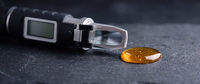 Refractometer measures sugar concentration in honey drop on dark slate background in laboratory setting