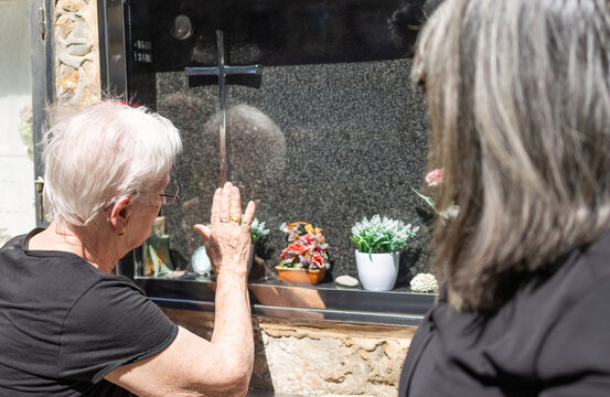 elderly woman placing her hand on a columbarium niche with her daughter , crying for a lost family member at a burial