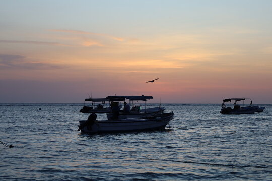 Scenic view of small fishing boat silhouettes floating on calm sea during colorful sunset or dusk, ideal for travel, leisure, and nature - colorful sky