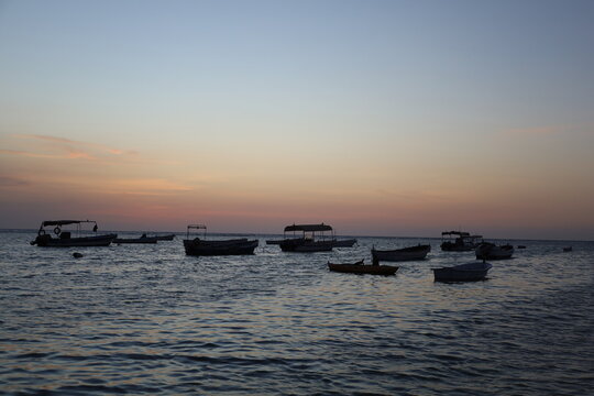 Scenic view of small fishing boat silhouettes floating on calm sea during colorful sunset or dusk, ideal for travel, leisure, and nature - colorful sky