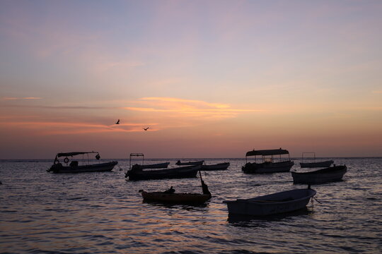 Scenic view of small fishing boat silhouettes floating on calm sea during colorful sunset or dusk, ideal for travel, leisure, and nature - colorful sky
