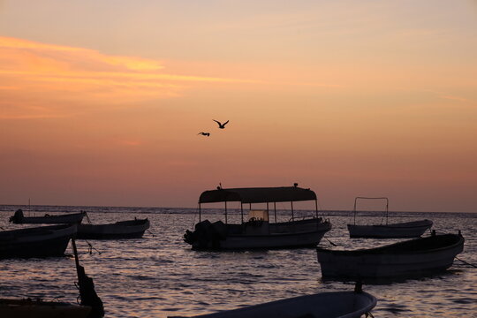 Scenic view of small fishing boat silhouettes floating on calm sea during colorful sunset or dusk, ideal for travel, leisure, and nature - colorful sky