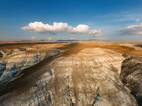 Aerial view of the arid, rugged landscape with rolling hills, layered sedimentary rock formations, and a vast horizon under a blue sky in Sivrihisar, Eskisehir, Turkey.