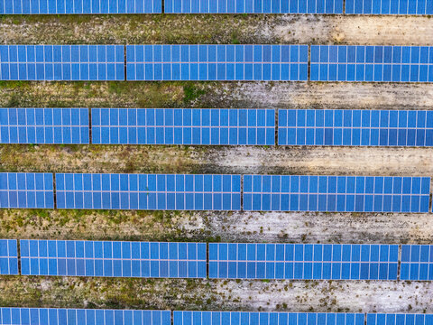 Aerial view of rows of blue photovoltaic solar panels arranged in a large field with patches of grass and soil in Wilmington, North Carolina, United States.