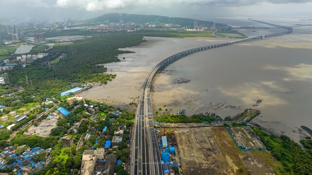 Aerial view of Atal Bihari Vajpayee Sewri-Nhava Sheva Atal Setu bridge spanning the bay with industrial coastal areas and greenery in the background, Mumbai, Maharashtra, India.
