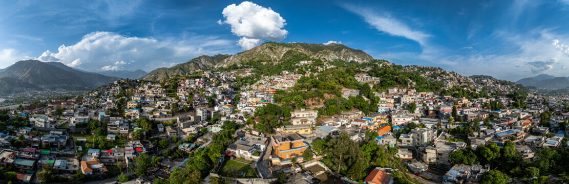 Aerial view of the dense residential buildings and lush green mountains surrounding the city of Muzaffarabad, Azad Kashmir, Pakistan.