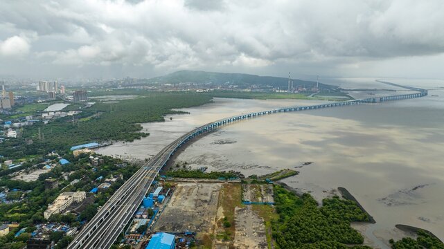 Aerial view of the Atal Bihari Vajpayee Sewri-Nhava Sheva Atal Setu bridge spanning the bay with lush mangroves and urban landscape under a cloudy sky in Mumbai, Maharashtra, India.