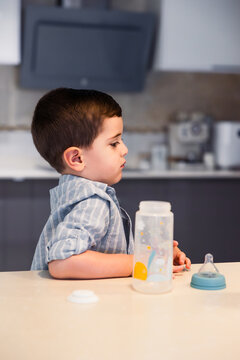Little boy waiting for baby bottle in kitchen