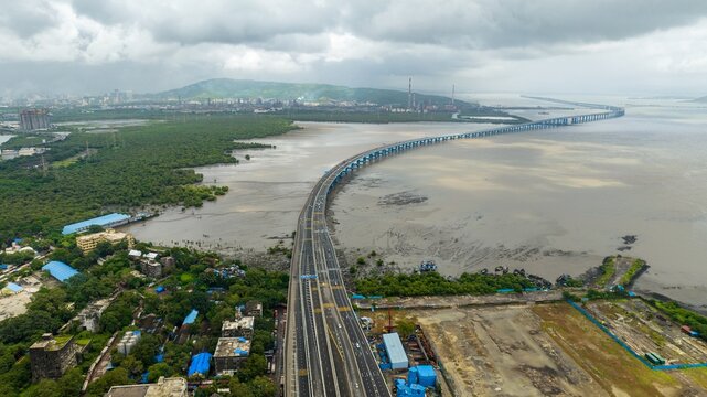 Aerial view of the Atal Bihari Vajpayee Sewri-Nhava Sheva Atal Setu bridge spanning the bay with lush mangroves, industrial skyline, and cloudy sky in Mumbai, Maharashtra, India.
