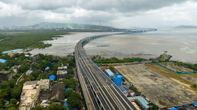 Aerial view of Atal Bihari Vajpayee Sewri-Nhava Sheva Atal Setu stretching across the bay with lush mangroves, urban infrastructure, and a cloudy sky in Mumbai, Maharashtra, India.