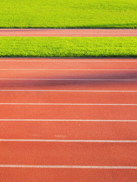 Red running track lanes with white lines next to bright green grass athletic field