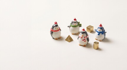 Obraz premium Minimalist Festive Composition with Small Ceramic Penguin Figurines Wearing Santa Hats and Colorful Scarves Arranged on a Neutral Cream Background with Decorative Gold Geometric Shapes for Christmas