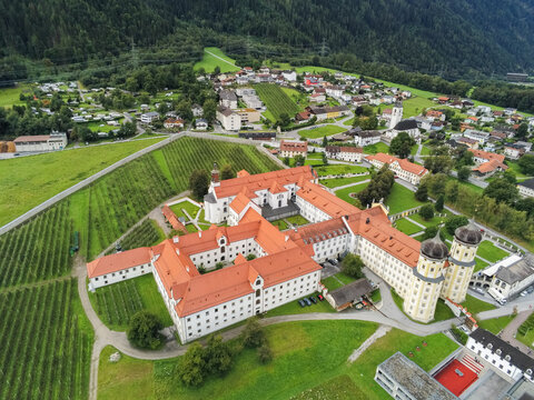 Aerial view of Stift Stams monastery with its distinctive red roofs, courtyards, and surrounding green fields in the alpine landscape of Stams, Tirol, Austria.