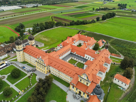 Aerial view of Stift Stams, a historic Cistercian monastery with onion-domed towers and red-tiled roofs, surrounded by lush green fields and agricultural land in Stams, Tirol, Austria.