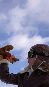 A happy child is playing with a wooden airplane outside in winter. A child with a toy airplane pretends to be a pilot. The concept of childhood dreams and freedom. Slow motion. Vertical video