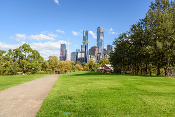 Fototapeta premium Paved footpath running between lawns in a public park in a city centre on a sunny autumn day. Modern high rise residential and office buildings are visible in background.