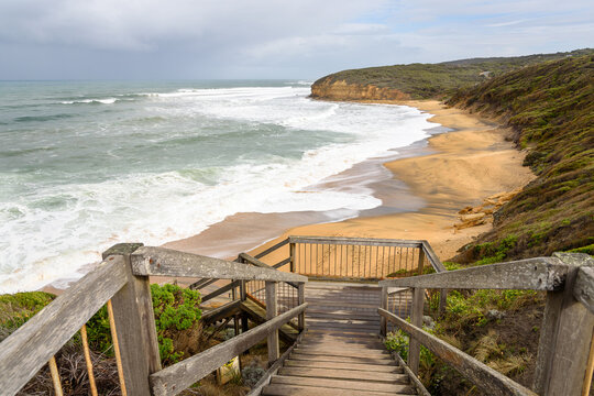 Deserted wooden staircase leading down to a deserted sandy beach hit by big waves on a cloudy autumn day