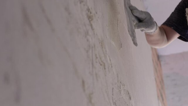 Worker smoothing plaster on wall with wide trowel
