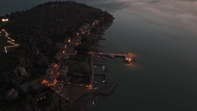 Aerial view of the illuminated Isola Maggiore pier and village on Lake Trasimeno at dusk in Tuoro sul Trasimeno, Umbria, Italy.