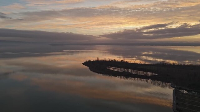 Aerial view of Isola Maggiore at sunset with calm waters reflecting the golden sky in Tuoro sul Trasimeno, Umbria, Italy.