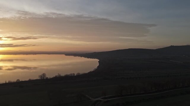 Aerial view of Isola Maggiore on Lake Trasimeno at sunset with golden light reflecting on the water and rolling hills in the background in Tuoro sul Trasimeno, Umbria, Italy.