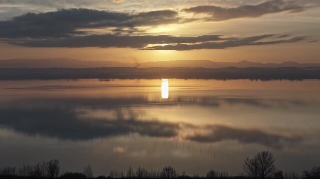 Aerial view of Isola Maggiore at sunset over Lake Trasimeno with golden light reflecting on the calm water surface in Tuoro sul Trasimeno, Umbria, Italy.