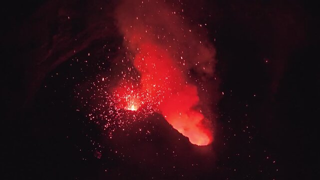 Aerial view of Stromboli volcano erupting at night with glowing lava and sparks against the dark sky in Stromboli, Sicily, Italy.