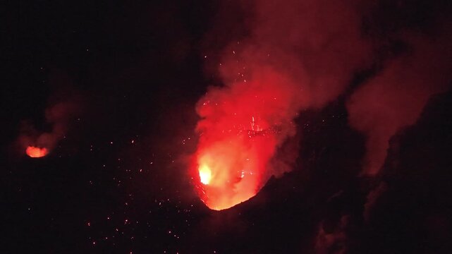 Aerial view of the Stromboli volcano erupting at night with glowing lava and sparks illuminating the dark sky in Stromboli, Sicily, Italy.