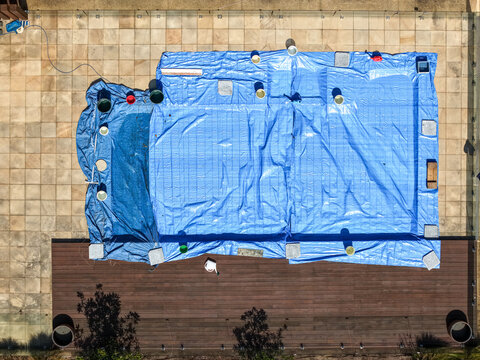 Aerial view of a swimming pool covered with a large blue tarp on a stone-tiled patio next to a wooden deck in Melbourne, VIC, Australia.
