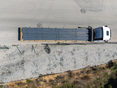 Aerial view of a white truck transporting a load of steel rebar on a paved road next to a cobblestone area in Istanbul, Istanbul, Turkiye.
