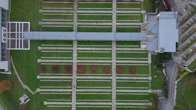 Aerial view of the monumental cemetery of Longarone with rows of white headstones and green grass in Longarone, Veneto, Italy.