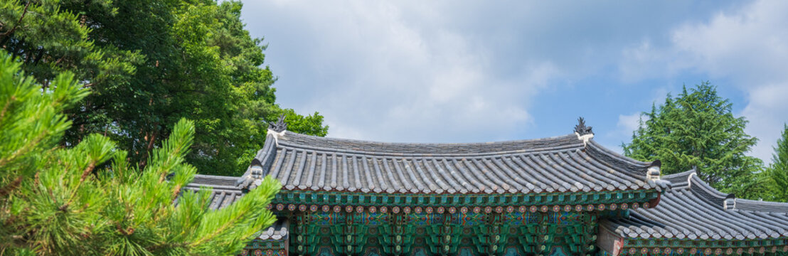 Traditional Korean temple tiled roof with elaborate dancheong patterns and dragon ridge ornaments under a blue sky in South Korea.