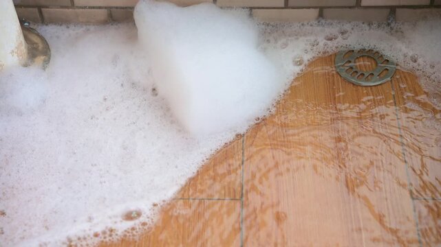 Soapy foam slowly draining through floor drain on wood patterned tile floor