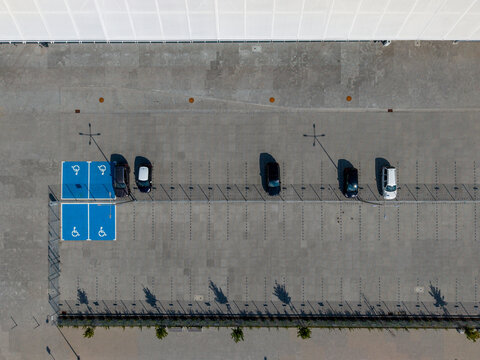 Aerial view of a parking lot featuring blue accessible parking spaces and several parked cars on a concrete surface in Opole, Opole Voivodeship, Poland.