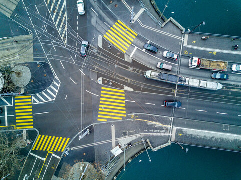 Aerial view of a busy urban intersection in Zurich with a tram crossing the bridge, yellow pedestrian crossings, and cars moving through the city center, Zurich, Zurich, Switzerland.