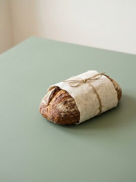 Fresh sourdough bread loaf wrapped in handmade paper with twine on green table. Crusty artisan loaf with copy space. Organic bakery and slow food concept. Rustic zero waste packaging.