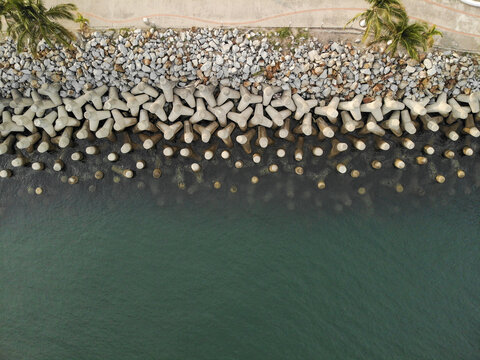 Aerial view of concrete tetrapods forming a breakwater along the coastline with a paved walkway and palm trees in La Cruz de Huanacaxtle, Nayarit, Mexico.